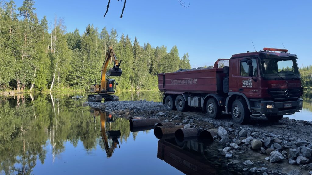 Kaivinkone ja kuorma-auto rakentamassa patoa